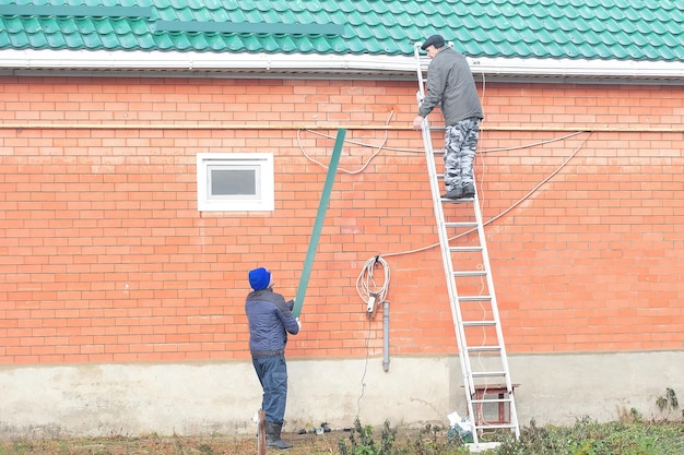 die familie macht das haus winterfest, die männer montieren schneefanggitter auf dem dach des hauses