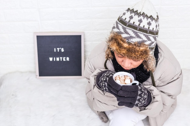 Draufsicht einer Frau mit Pufferjacke und Strickmütze, die im Winter ein heißes Getränk genießt