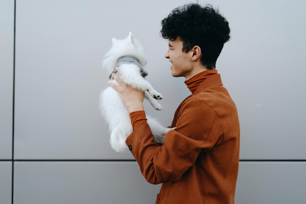 Foto ein junger mann hält einen flauschigen weißen hund vor einem neutralen grauen hintergrund