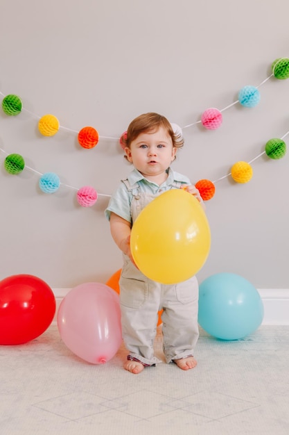 Foto ein lustiger kaukasischer junge feiert seinen ersten geburtstag, ein kleinkind spielt mit ballons.