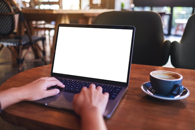 Eine Frau benutzt und schreibt auf einer Laptop-Tastatur mit einem leeren weißen Desktop-Bildschirm in einem Café