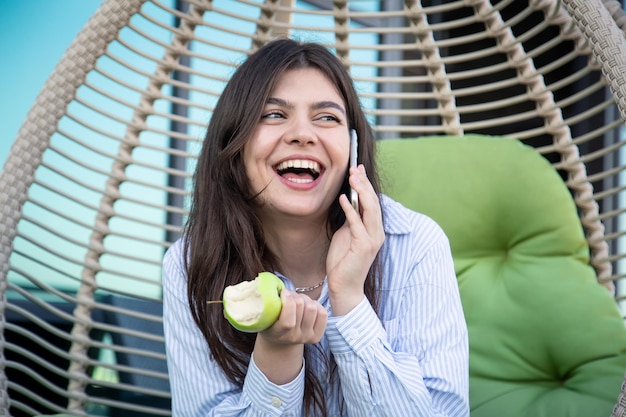 Eine junge Frau isst einen Apfel mit einem Smartphone in der Hand