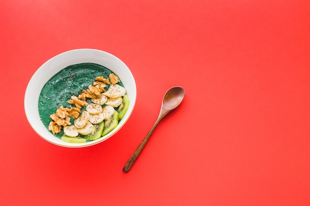 Eine Spirulina-Smoothie-Schüssel mit Bananen-, Walnuss-, Kiwi- und Chiasamen auf rotem Hintergrund