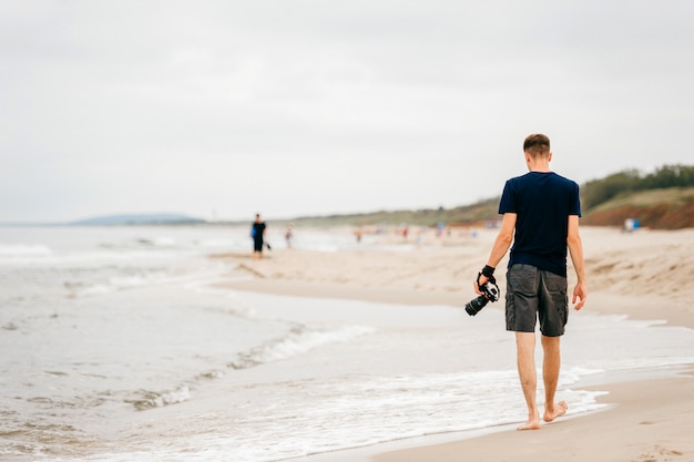 Foto einsamer fotograf mit einer kamera in seiner hand, die entlang meer geht.