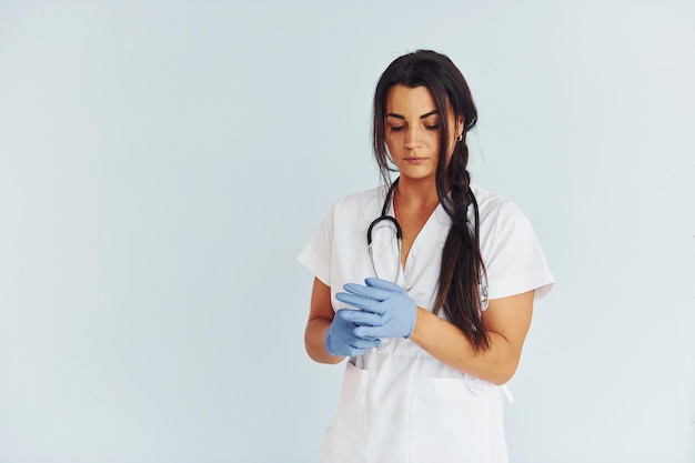 Em pé contra o fundo branco Jovem médica de uniforme está dentro de casa