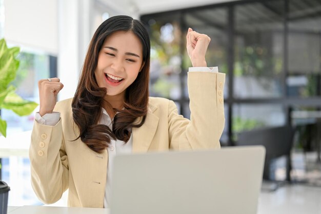 Foto empresária asiática feliz e alegre olhando para a tela do laptop comemorando seu sucesso