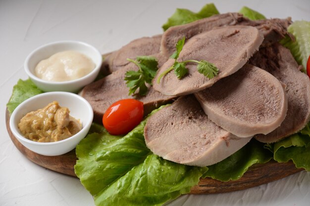 Foto fatias de língua de carne em uma travessa com folhas de alface, tomate cereja e mostarda de dijon em um fundo de madeira