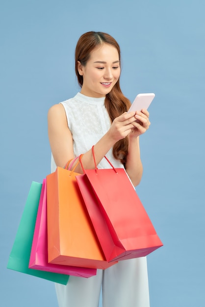 Foto fazendo a conexão de varejo. mulher jovem e bonita com sacolas de compras usando seu telefone inteligente com um sorriso em pé