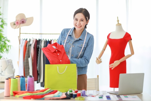 Feche a foto de uma jovem linda estilista asiática em pé e empacotando roupas para enviar ao consumidor de outros países pela mente de serviço.