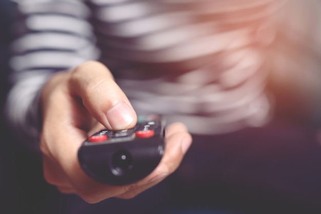 Feche o controle remoto da televisão nas mãos de um homem casual apontando para o aparelho de TV e ligando-o ou desligando-o