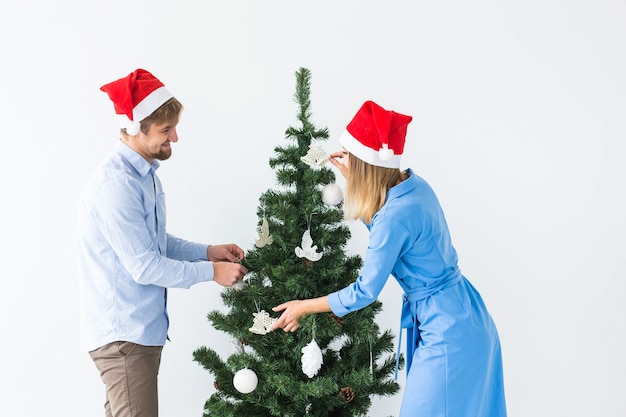 Feiertage und festliches Konzept - Junges Familienpaar in Weihnachtsmützen, die den Weihnachtsbaum schmücken