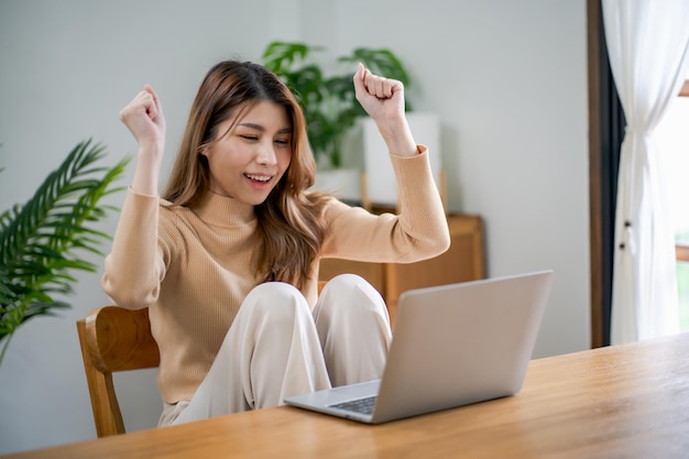 Foto feliz jovem asiática trabalhando com sucesso com laptop verificando feliz parabéns receba boas notícias jovem asiática se sente animada e colega estudante passou no exame