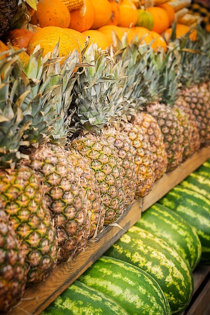 Fila de abacaxis maduros no mercado local de frutas com melancia e laranjas como comida saudável de verão