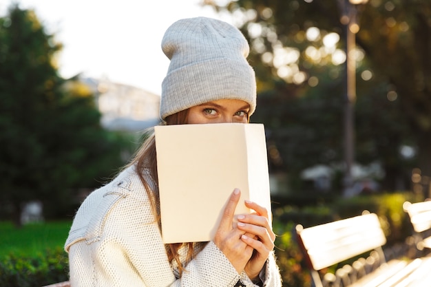 Foto de uma mulher ruiva caminhando ao ar livre, segurando o caderno cobrindo o rosto.