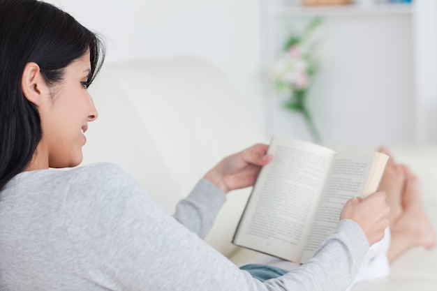 Foto frau, die ein buch beim legen auf ein sofa liest