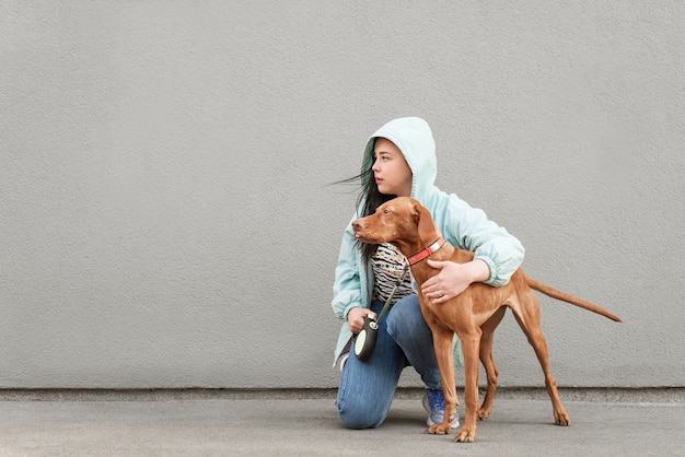 Foto frau hält einen hund an der leine, sitzt auf dem hintergrund einer grauen wand und schaut zur seite.