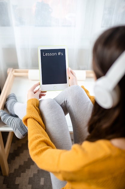 Foto frau in weißen drahtlosen kopfhörern hält weißes tablett mit stift. home office während der selbstisolation, arbeiten von zu hause aus. online-bildung, e-learning während der quarantäne.