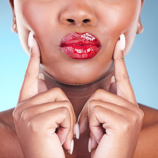 Frau küsst sich und roter Lippenstift und Schönheitshände berühren Gesicht und Make-up-Nahaufnahme isoliert auf blauem Hintergrund Modell kühnes und kosmetisches Produkt auf Lippen Schmollmund und Mund Maniküre und Glanz im Studio