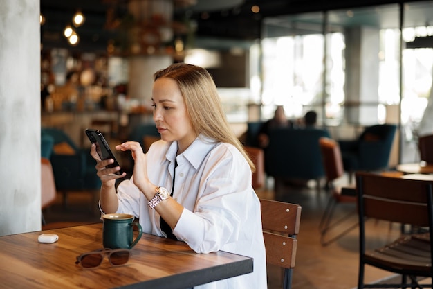 Frau tippt Textnachricht auf Smartphone, während sie in einem Café sitzt