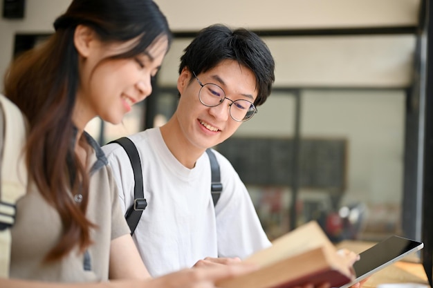 Foto fröhlicher asiatischer college-student, der seiner freundin am wochenende in einem café geschichte beibringt