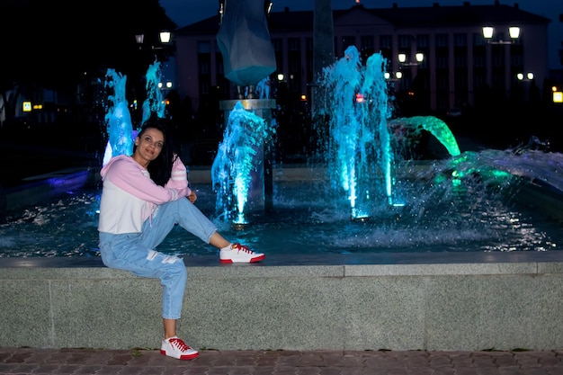 Fröhliches lächelndes Mädchen sitzt nachts am Brunnen