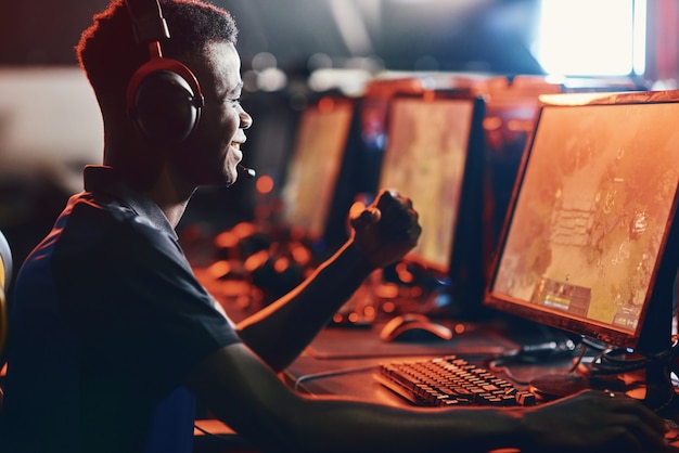 Gewinnen. Seitenansicht eines aufgeregten afrikanischen Kerls, männlicher professioneller Spieler mit Kopfhörern, der den Erfolg feiert, während er am eSport-Turnier teilnimmt. Leute, die Online-Videospiele spielen