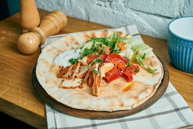 Foto giroscópios gregos com iogurte, frango, pepino e tomate em uma mesa de madeira. comida de rua