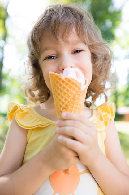 Glückliches Kind, das im Sommerpark Eis im Freien isst