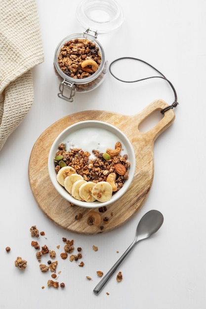 Foto granola com banana e nozes em uma tábua de madeira em uma mesa branca com um guardanapo e colher