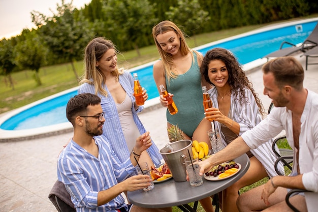 Gruppe junger Leute, die mit Apfelwein am Pool im Garten jubeln