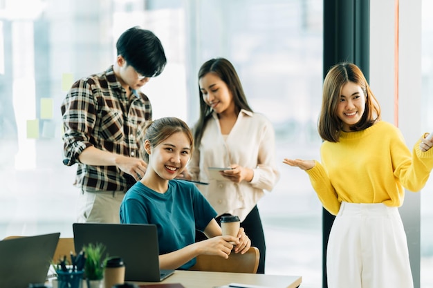 Foto gruppe von vier glücklichen jungen asiatischen geschäftsleuten, teamkollegen, die im büro über geschäfte diskutieren.