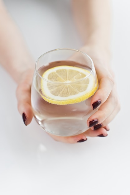 Hände, die ein Glas klares Wasser mit Zitrone halten.