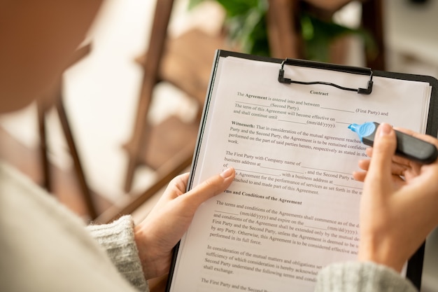 Foto hände einer jungen bewerberin mit blauem textmarker, die nach dem interview mit dem arbeitgeber den vertrag durchsieht, bevor sie ihre unterschrift setzt