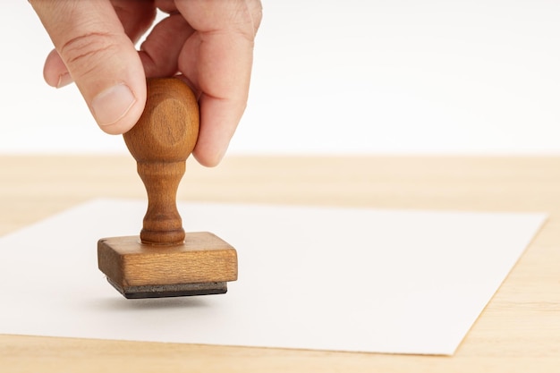 Foto hand hält einen gummi-stempel und leeres papier auf einem holztisch weißer hintergrund kopierplatz