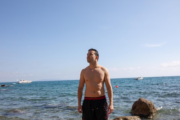 Foto hemdloser mann steht am strand gegen den blauen himmel