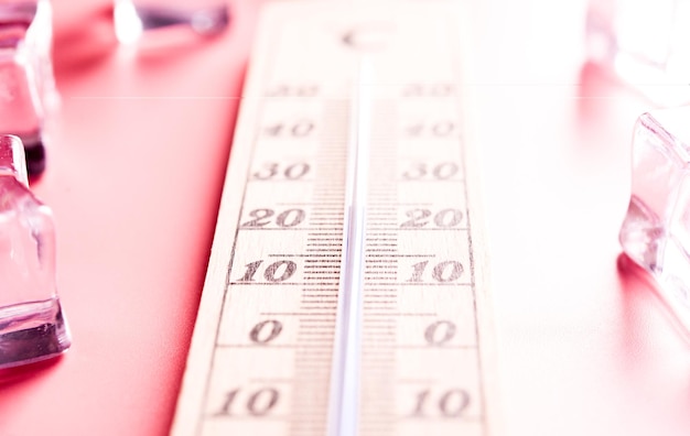 Holzthermometer zeigt hohe Temperaturen in Fahrenheit oder Celsius auf hellrosa Hintergrund mit Eis