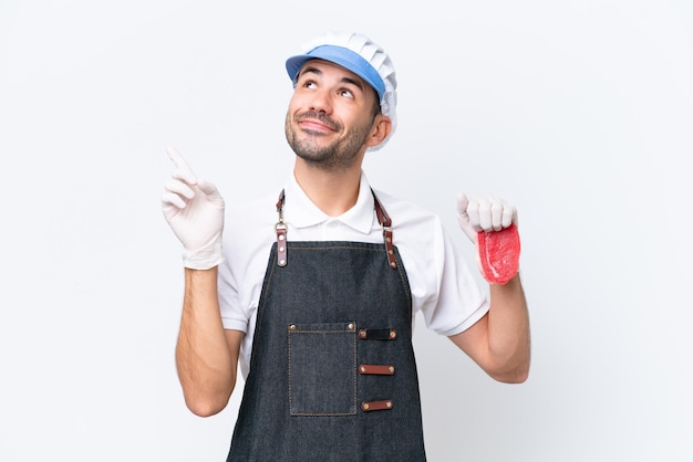 Homem caucasiano de açougueiro vestindo um avental e servindo carne fresca cortada sobre fundo branco isolado apontando para cima uma ótima idéia