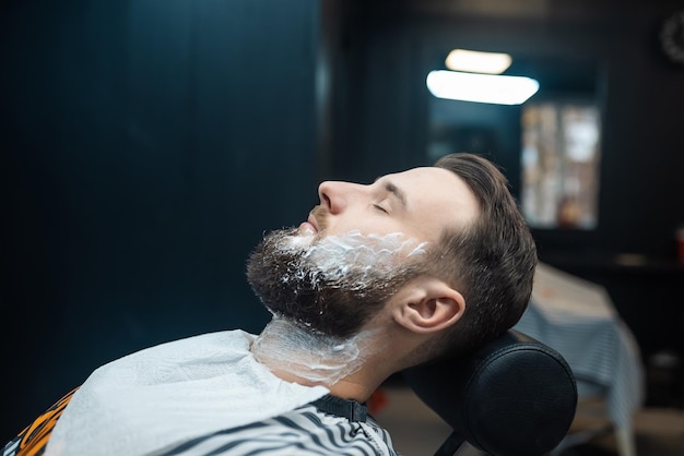 Homem com espuma de barbear no rosto em uma barbearia vista de perto