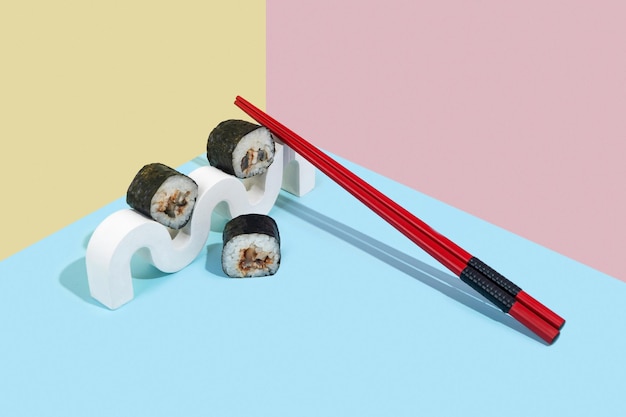 Foto hosomaki-sushi-rollen mit aal auf einem weißen gipsständer auf einem farbenfrohen, einfarbigen hintergrund, blau, rosa, gelb