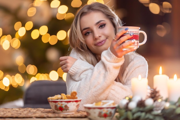 Jovem linda em uma atmosfera de Natal segurando uma xícara com café ou chá