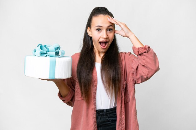 Foto jovem mulher árabe segurando o bolo de aniversário sobre fundo branco isolado com expressão de surpresa