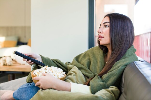 Foto jovem mulher bonita assistindo a um filme e sentada em um sofá em casa