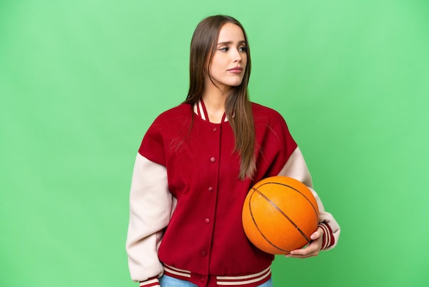 Jovem mulher bonita jogando basquete sobre fundo croma chave isolado, olhando para o lado