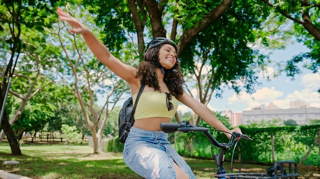 Foto jovem mulher latina em capacete protetor está andando de bicicleta ao longo da ciclovia em um parque da cidade