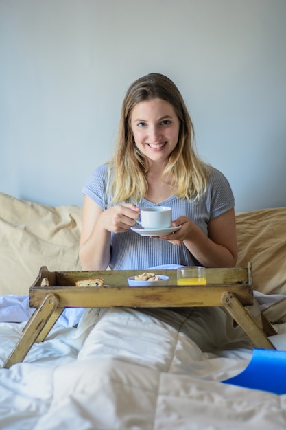 Jovem mulher na cama tomando café da manhã