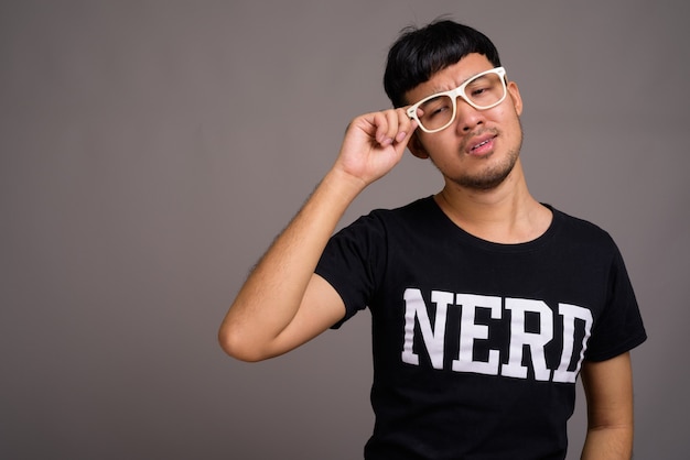 Foto jovem nerd asiático usando óculos contra o cinza