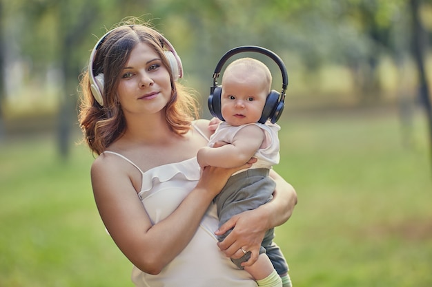 Junge Mutter und Baby hören Musik über drahtlose Kopfhörer