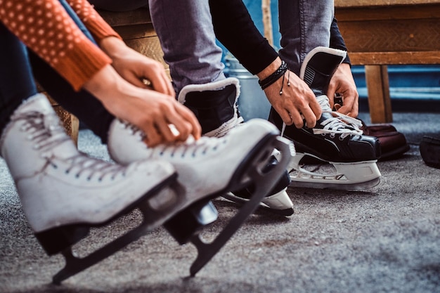 Junge Paare, die sich auf ein Skaten vorbereiten. Nahaufnahme ihrer Hände, die in einer Umkleidekabine Schnürsenkel von Eishockeyschlittschuhen binden