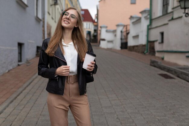 Junge Touristin geht mit einer Tasse Kaffee in den Händen und einem Telefon durch die Stadt