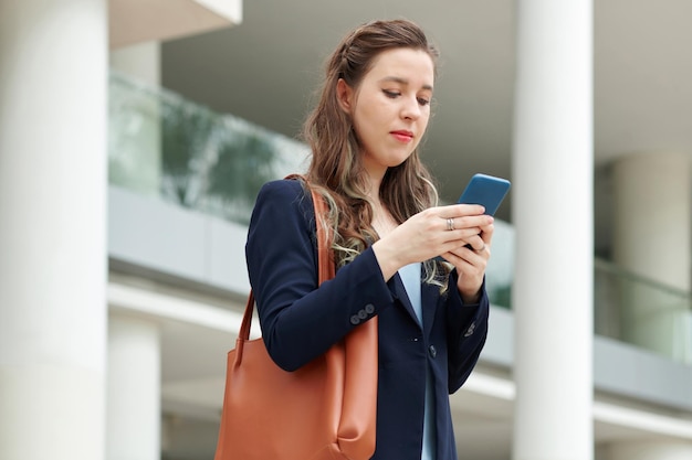 Junge Unternehmerin steht im Freien und überprüft Textnachrichten auf ihrem Handy